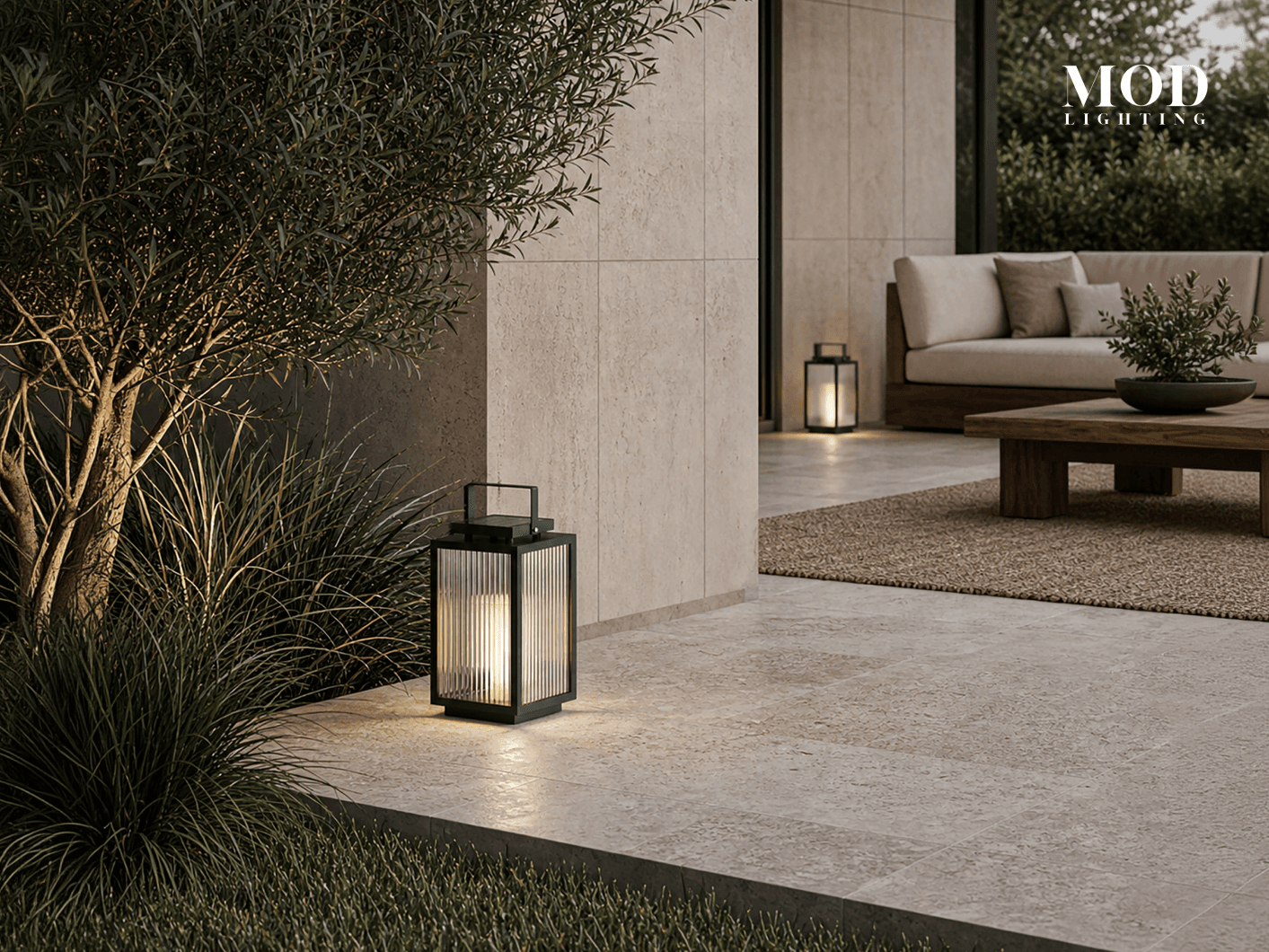 Beacon black solar lantern lit on a patio beside ornamental grasses, with a lounge seating area behind